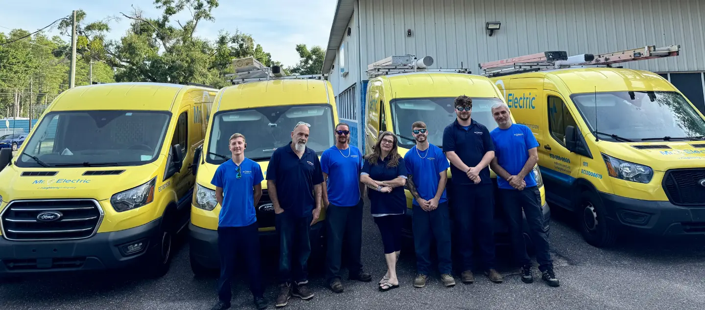 The Mr. Electric of Tampa Bay team in front of yellow Mr. Electric utility vehicles.